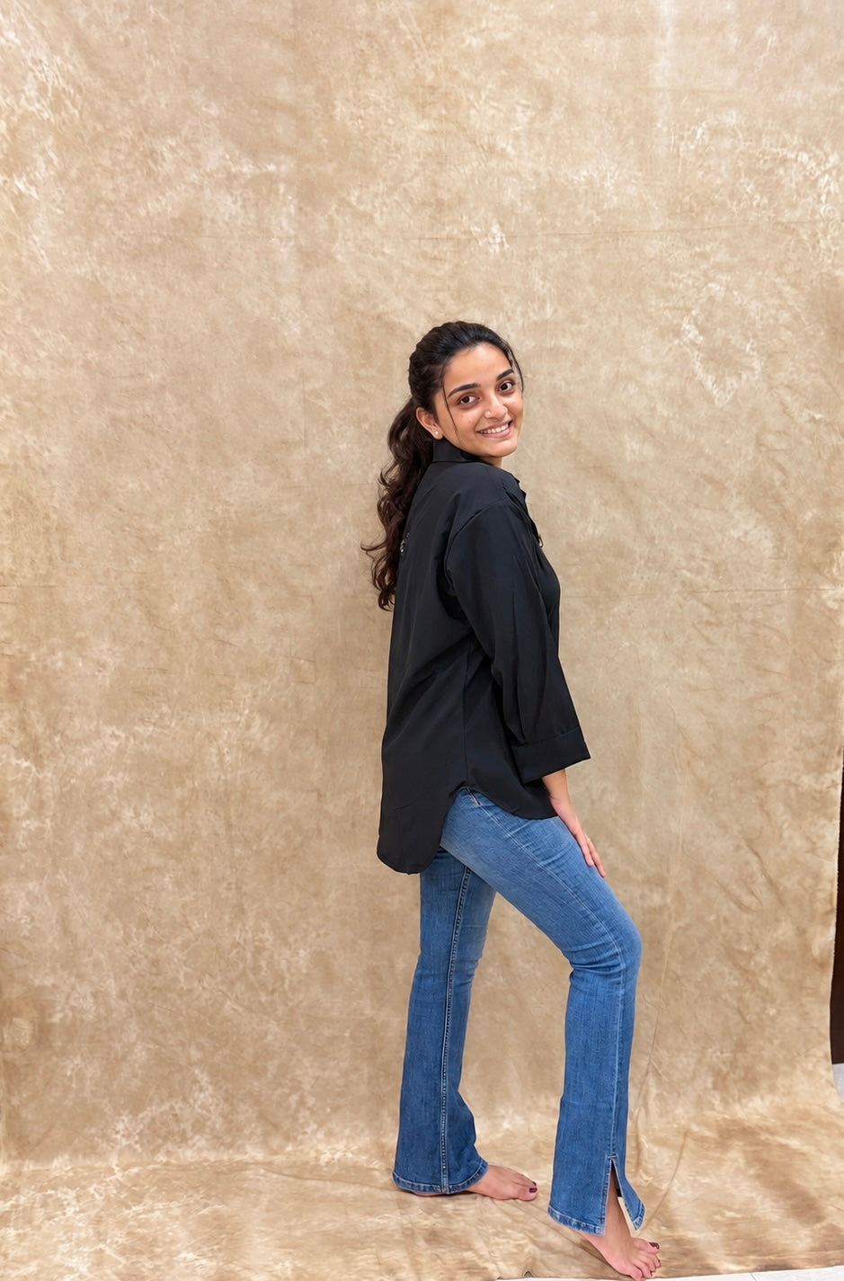 Side view of black relaxed-fit shirt with rolled cuffs and flared denim