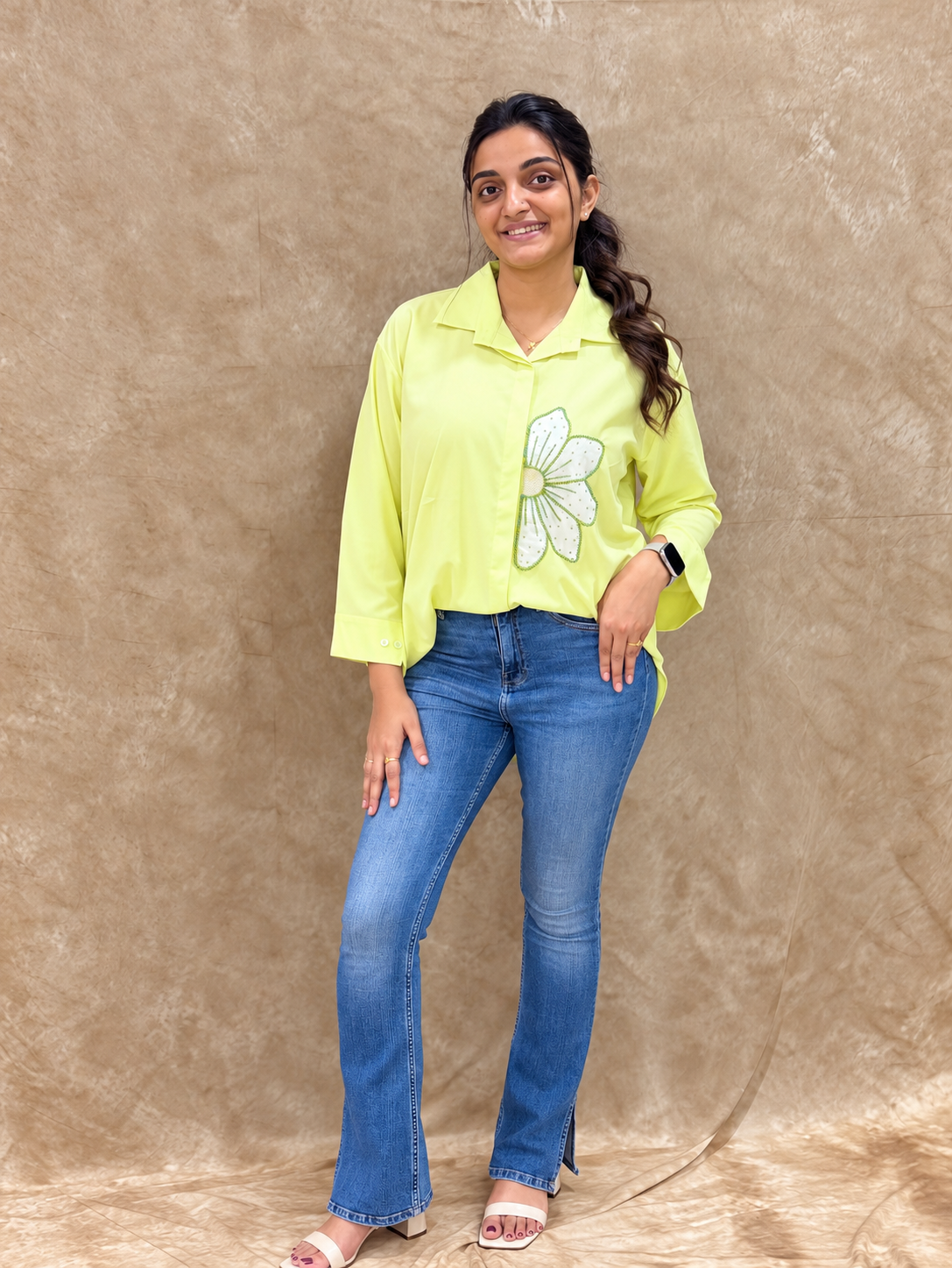 Woman in lime green shirt with white hand-embellished flower motif, styled with flared blue jeans